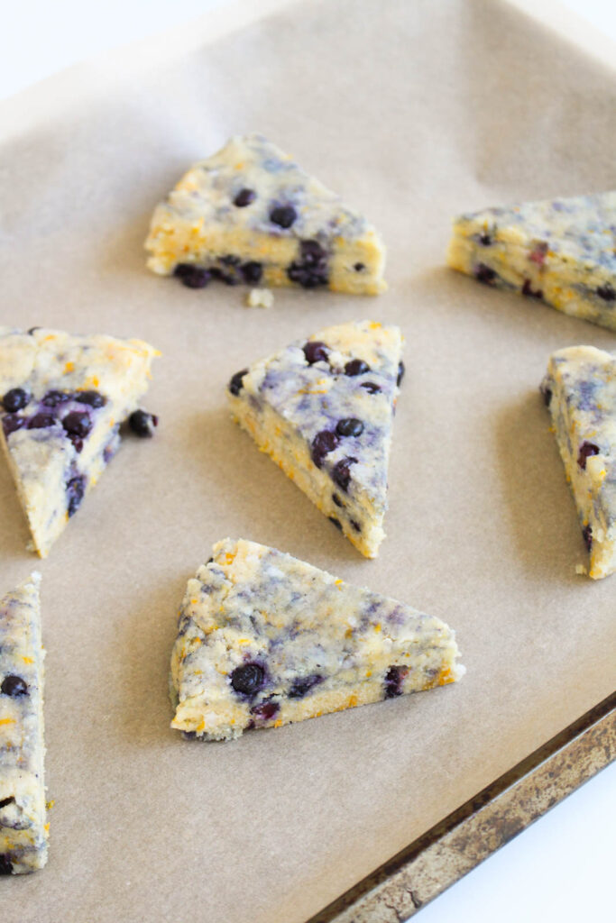 Scones are cut into triangles, lying on top of a baking sheet before going into the oven.