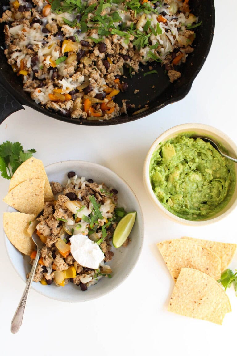 overhead view of taco skillet, served in a white bowl, with a bowl of guacamole and chips on the side.